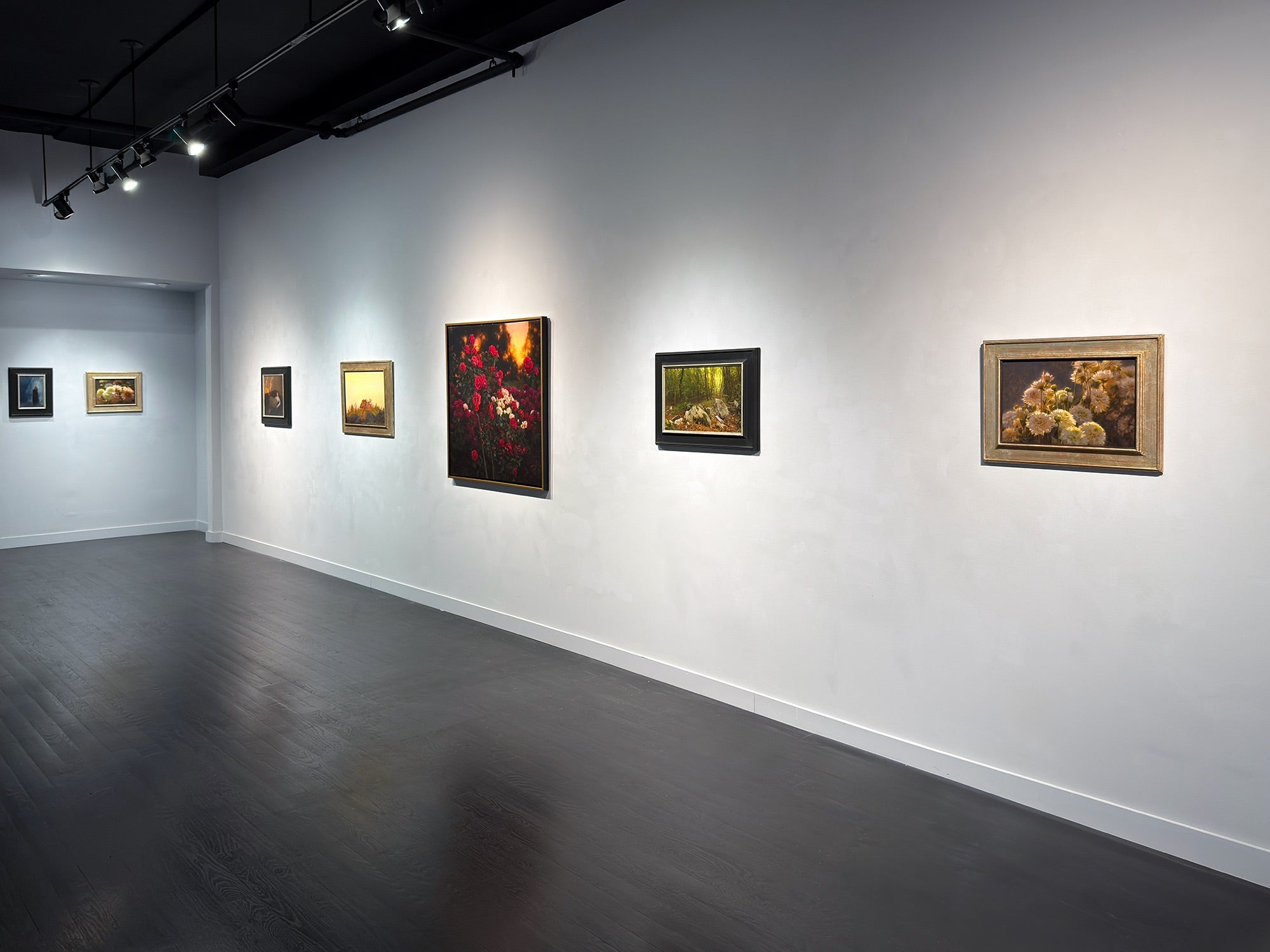 Art gallery with various framed paintings on a white wall.